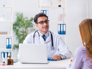 Doctor in a white coat sitting at a desk, speaking to a patient.