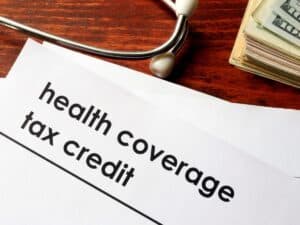 Document labeled 'Health Coverage Tax Credit' with a stethoscope and cash on a wooden desk.